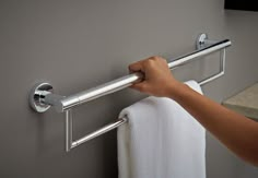 a person holding onto a towel rack in a bathroom with gray walls and white towels