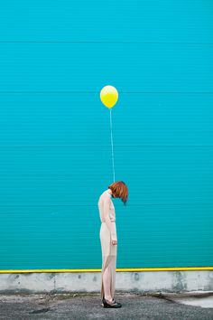 a woman holding a yellow balloon in front of a blue garage door with her head down