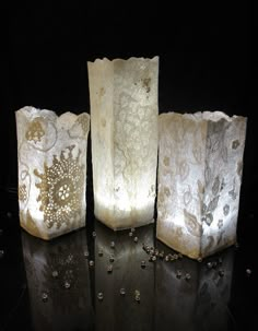 three white vases sitting next to each other on a black surface with beads all around them