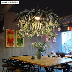 a dining room table and chairs with plants hanging from the chandelier above it