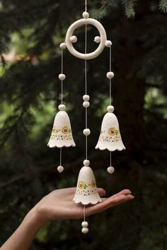 a hand holding a white bell wind chime with bells hanging from it's sides