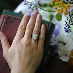 a woman's hand with a ring on her finger next to a book and flowers