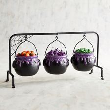 three halloween caulders with candy in them on a metal stand against a marble wall