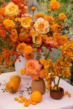 an arrangement of flowers and oranges on a table