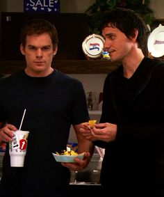 two men standing next to each other holding food in their hands and looking at the camera