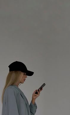 a woman wearing a black hat looking at her cell phone while standing in front of a gray wall