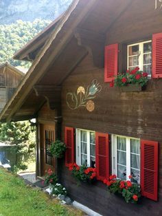 a wooden house with red shutters and flowers on the windows