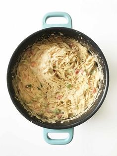 a pan filled with noodles and vegetables on top of a white table next to a knife