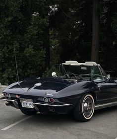 an old black corvette convertible parked in a parking lot with trees behind it and a white top