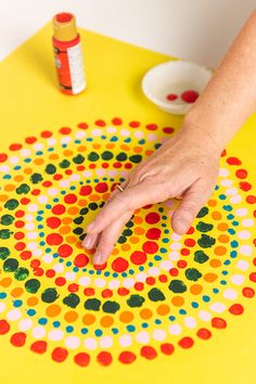 a person's hand is touching the center of a colorful dot pattern on a yellow surface