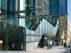 people walking on the sidewalk in front of an office building with glass walls and stairs