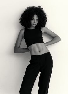 a black and white photo of a woman with her arms on her hips, leaning against a wall