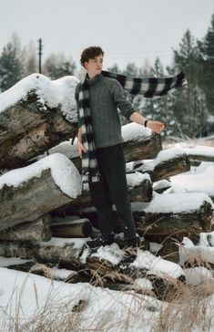 a young man standing on top of snow covered ground next to logs and tree trunks