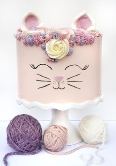 a cake decorated with flowers and yarn on top of a white table next to balls of yarn