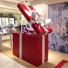 a red gift box with white ribbon and bow on display in a retail store lobby