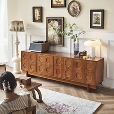 a woman sitting on a chair in front of a wooden dresser with pictures above it