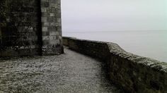 an open door on the side of a stone wall by the ocean with water in the background