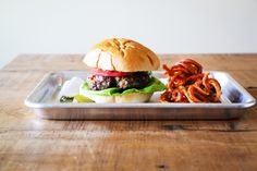 a plate with a hamburger and some onion rings on it, sitting on a wooden table