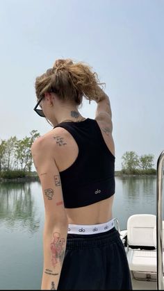 a woman with tattoos on her arm standing next to a body of water and boat