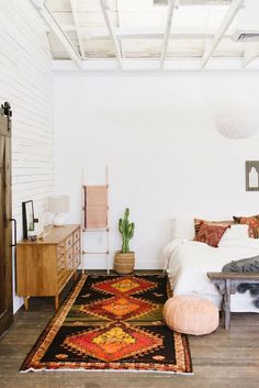 a room with a bed, dresser and rug on the floor in front of it