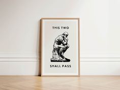 this two shall pass poster hangs on the wall in an empty room with wood flooring