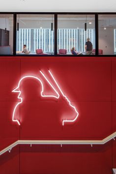 a neon sign on the side of a building with people sitting at tables in the background