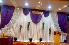 the stage is decorated with purple and white drapes, floral arrangements, and candles