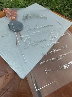 two clear acrylic wedding cards sitting on top of a wooden table in the grass