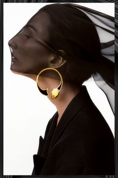 a woman wearing large gold hoop earrings with a black veil over her head in front of a white background