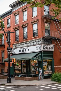 people walking on the sidewalk in front of an old brick building that has been converted into a deli