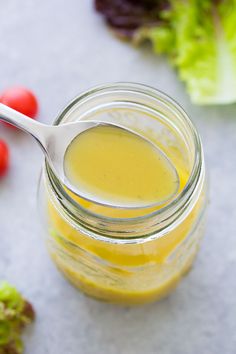 a spoon in a jar filled with mustard next to lettuce and cherry tomatoes