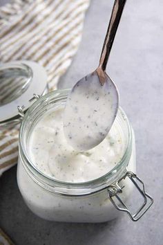 a spoon full of yogurt sitting on top of a glass jar filled with liquid