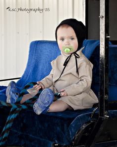 a baby sitting on top of a blue chair with a pacifier in it's mouth