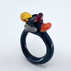 "Welcome to Hidden Glass Atelier! Glad you have found me  ✦ DESIGN    ✧ This ring is recognised as one of the finalists of the Venice Design Week jewellery exhibition.     ✧ Ring crown: floral shaped petal cluster elements inspired by traditional Venetian goblet flat \"ear\" shaped decoration    ✧ Ring band: hunky black ring band creating a modern funky look    ✧ Silver leaf: the silver leaf is added to the surface of the glass. Through the oxidisation process by the flame, the oxidised silver changed the original color of the black glass, leaving a hint of mysterious blue and green.     ✧ Styling: This original unique ring is definitely a statement piece. It is easy to wear up or down with a casual outfit or for a special occasion.     ✧ Durability: All the glass jewellery pieces are temp Unique Luxury Glass Jewelry, Full Glass Rings, Black Ring Band, Red Black Flower, Black Band Ring, Ring Crown, Jewellery Exhibition, Glass Ring, Contemporary Ring