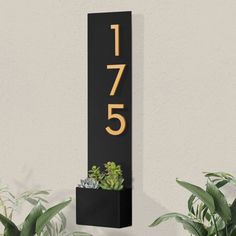 a house number sign mounted to the side of a wall next to potted plants