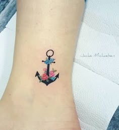 an anchor tattoo with flowers on the side of the ankle, and a ring in the middle