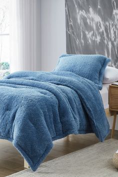 a bed with a blue comforter on top of it next to a book shelf