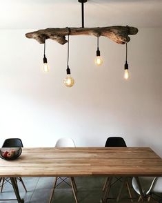 a wooden table with four lights hanging from it's ceiling and some chairs around it