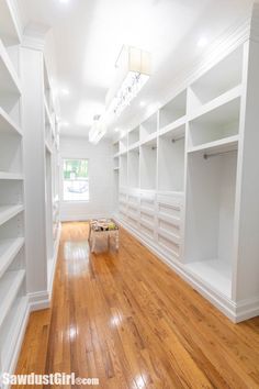 an empty walk in closet with white shelving and wood flooring on the side