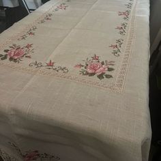 the table cloth has been embroidered with pink roses on it and is sitting in front of a window