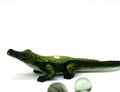 a toy alligator sitting next to two marbles on a white surface with one green and the other gray