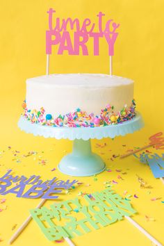 a birthday cake with sprinkles and candles on a yellow tablecloth surrounded by confetti