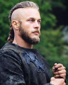 a man with long hair and braids standing in front of trees