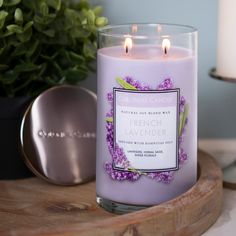 a lavender candle sitting on top of a wooden tray next to a potted plant