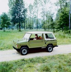 an old green jeep is parked on the side of a road in front of some trees