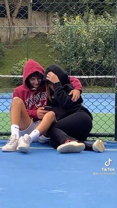 two people sitting on top of a tennis court with their arms around each other,