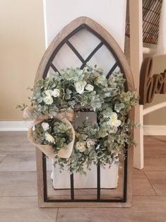 a wreath with white flowers and greenery hangs on the wall next to a window