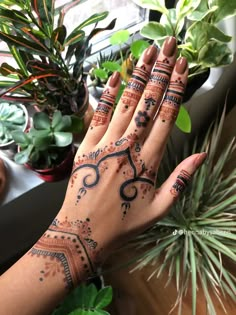 a woman's hand with henna tattoos on it and plants in the background