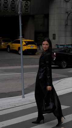 a woman walking across a street holding onto a black handbag in her right hand