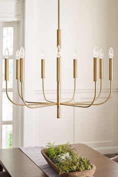 a chandelier hanging over a dining room table with moss in the center and candles on it